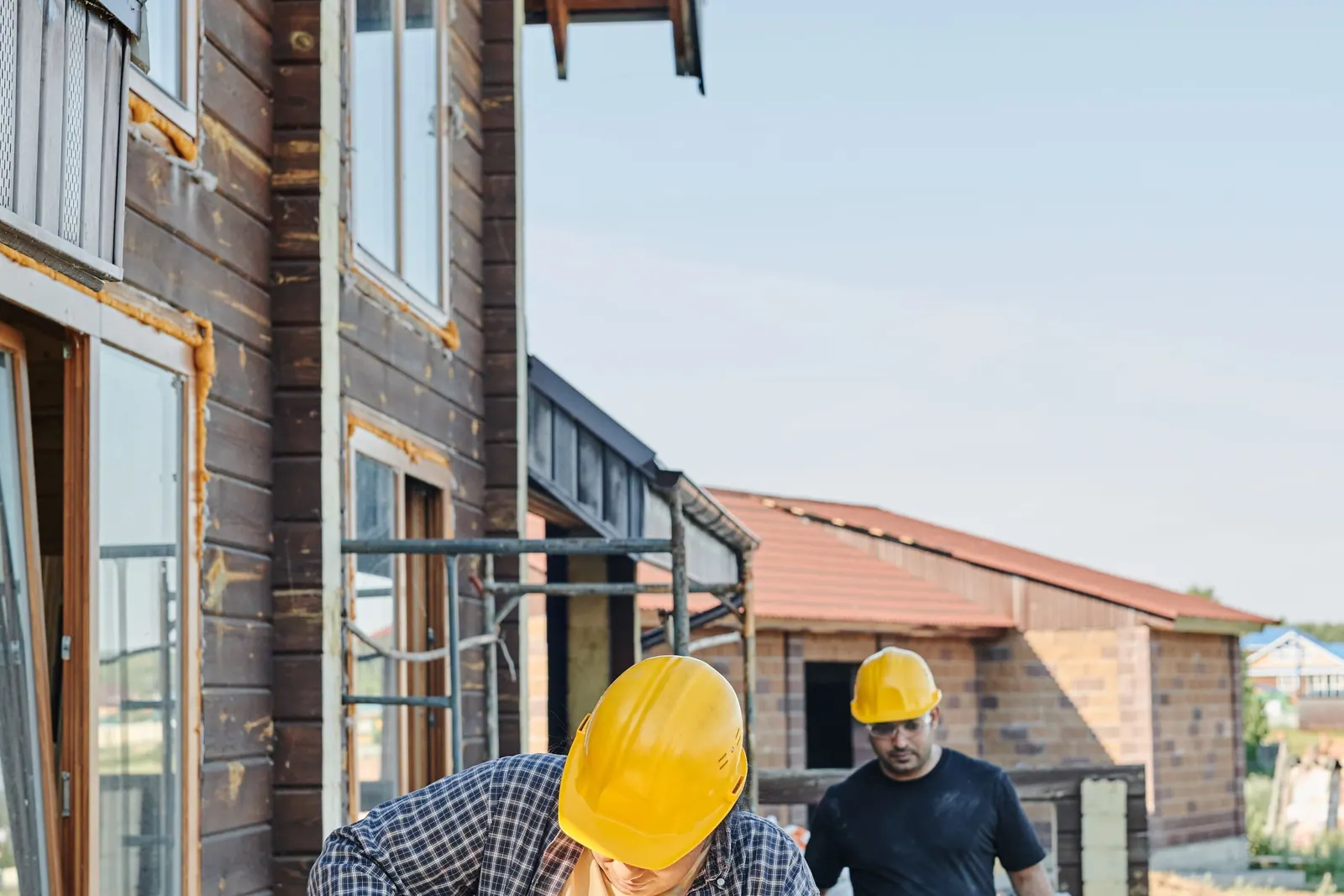 Two construction workers in hard hats at a timber-frame building site